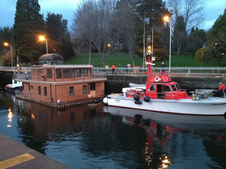 CASCADE towing a houseboat through a lock at dusk